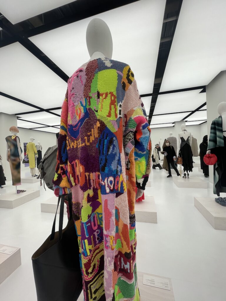 A vibrant, multicolored coat displayed in a LOEWE exhibition space , an inspiring piece that echoes Stylo Tokyo's approach to color analysis and styling with a bold, artistic sensibility.